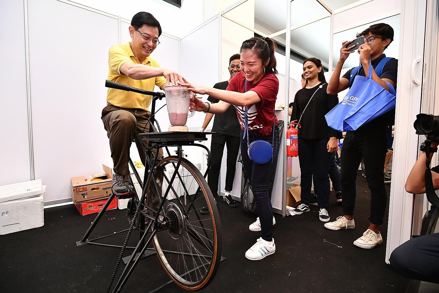 Finance Minister Heng Swee Keat cycling on a blender bike to make banana berry shake, with assistance from financial adviser Tan Ling, 25, who was helping out at the booth at the Tampines cycling path completion and ground-breaking ceremony at Our Ta