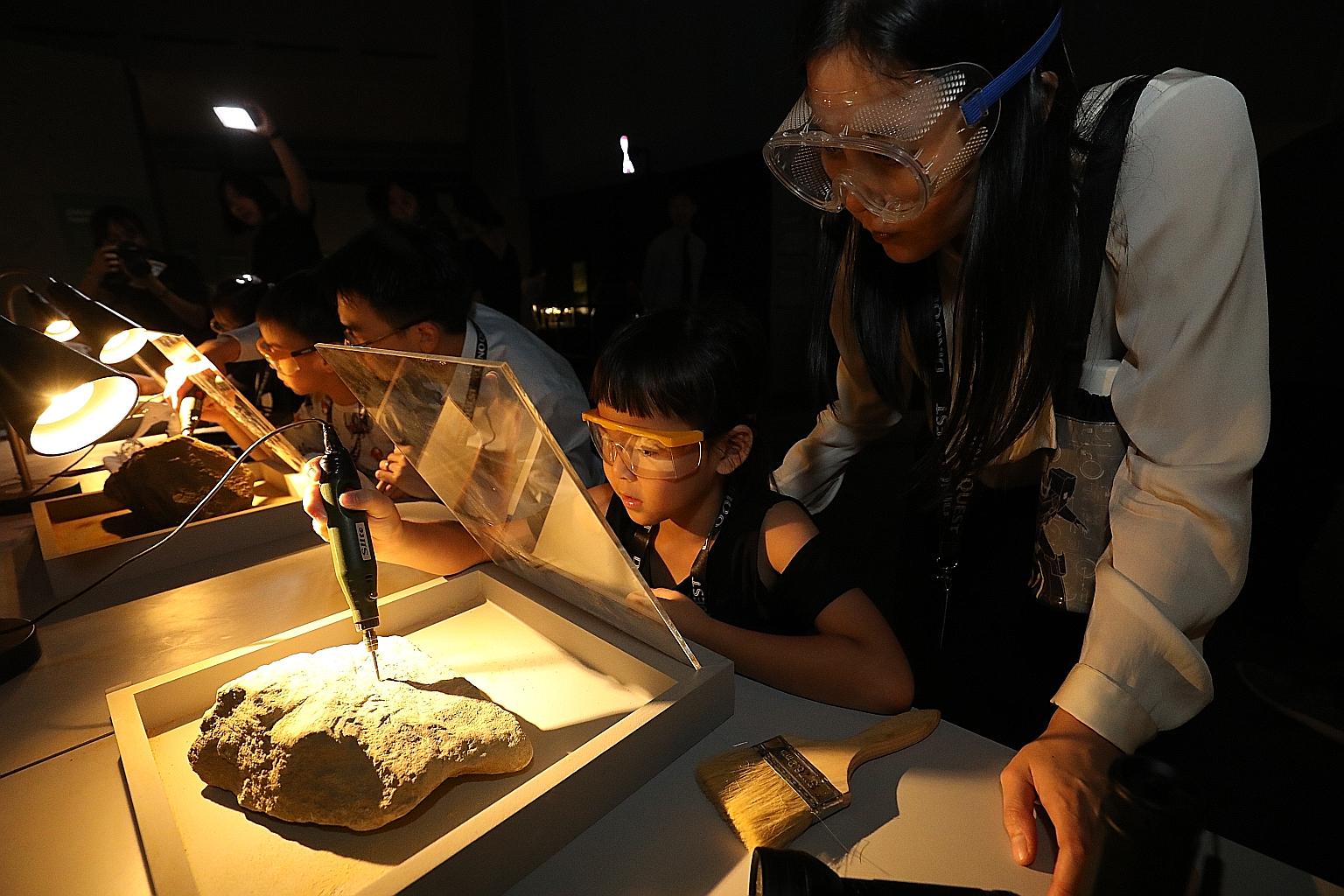 Visitors drilling into rocks to uncover fossils in a hands-on activity at the DinoQuest exhibition in Science Centre Singapore yesterday. The exhibition, which uses digital technology such as holograms, will be open to the public from next Saturday t