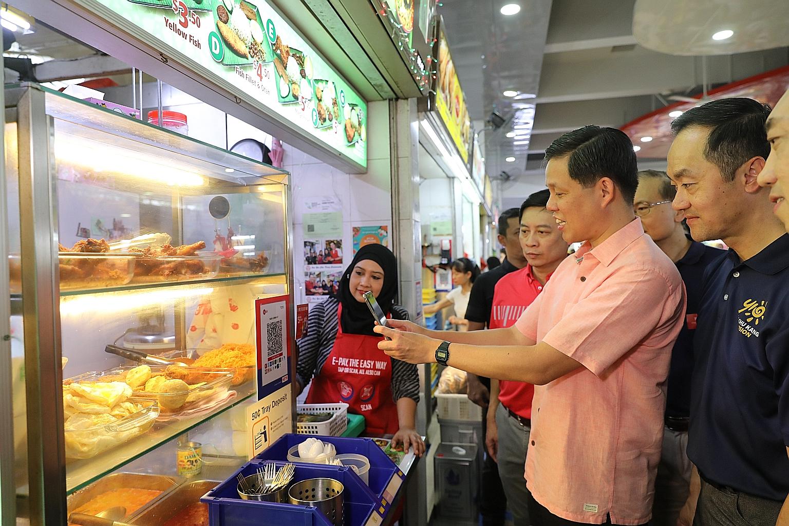 Minister for Trade and Industry Chan Chun Sing scanning the QR code at 49-year-old Madam Siti Naquiah's (left) nasi lemak stall in Ang Mo Kio yesterday, with Senior Minister of State for Trade and Industry Koh Poh Koon (right) looking on.