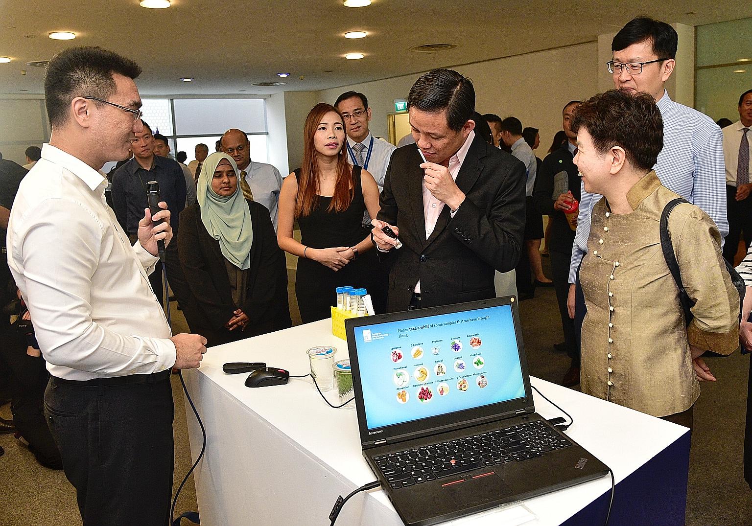 Research fellow and former A*Star scholarship recipient Andy Ng Yao Zong (left) watching as Trade and Industry Minister Chan Chun Sing takes a whiff of a fragrance produced by bio-engineered yeast cells. With them are (from right) A*Star chairman Cha