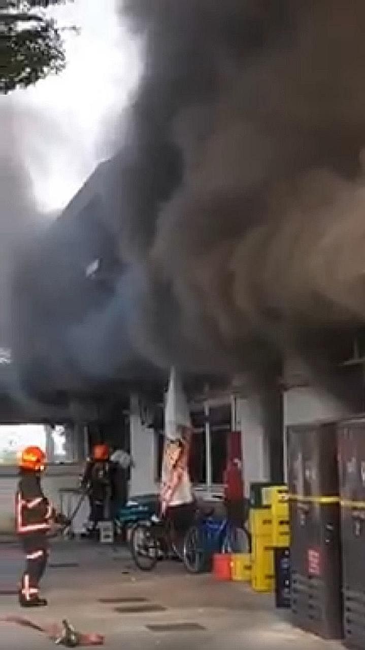 Above: Online footage shows black smoke billowing from the windows of the Jurong East coffee shop as firefighters tackle the blaze. Left: The fire involved the contents of a kitchen in the coffee shop.