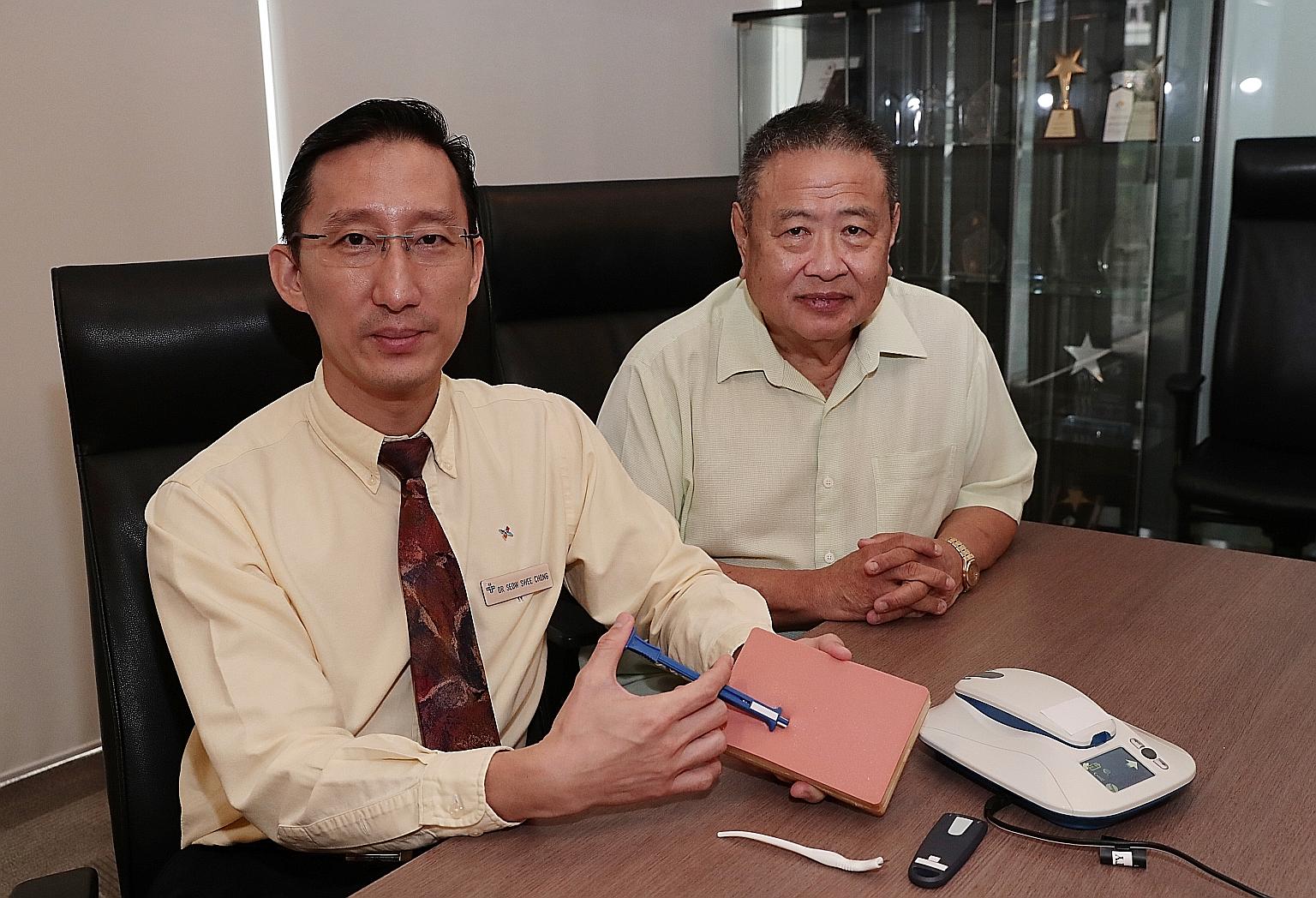 Dr Seow Swee Chong (left), a senior consultant at the National University Heart Centre's Department of Cardiology, and his patient Ng Kok Seng, 65, who has an Insertable Cardiac Monitor implanted in his chest. In the picture, Dr Seow is demonstrating