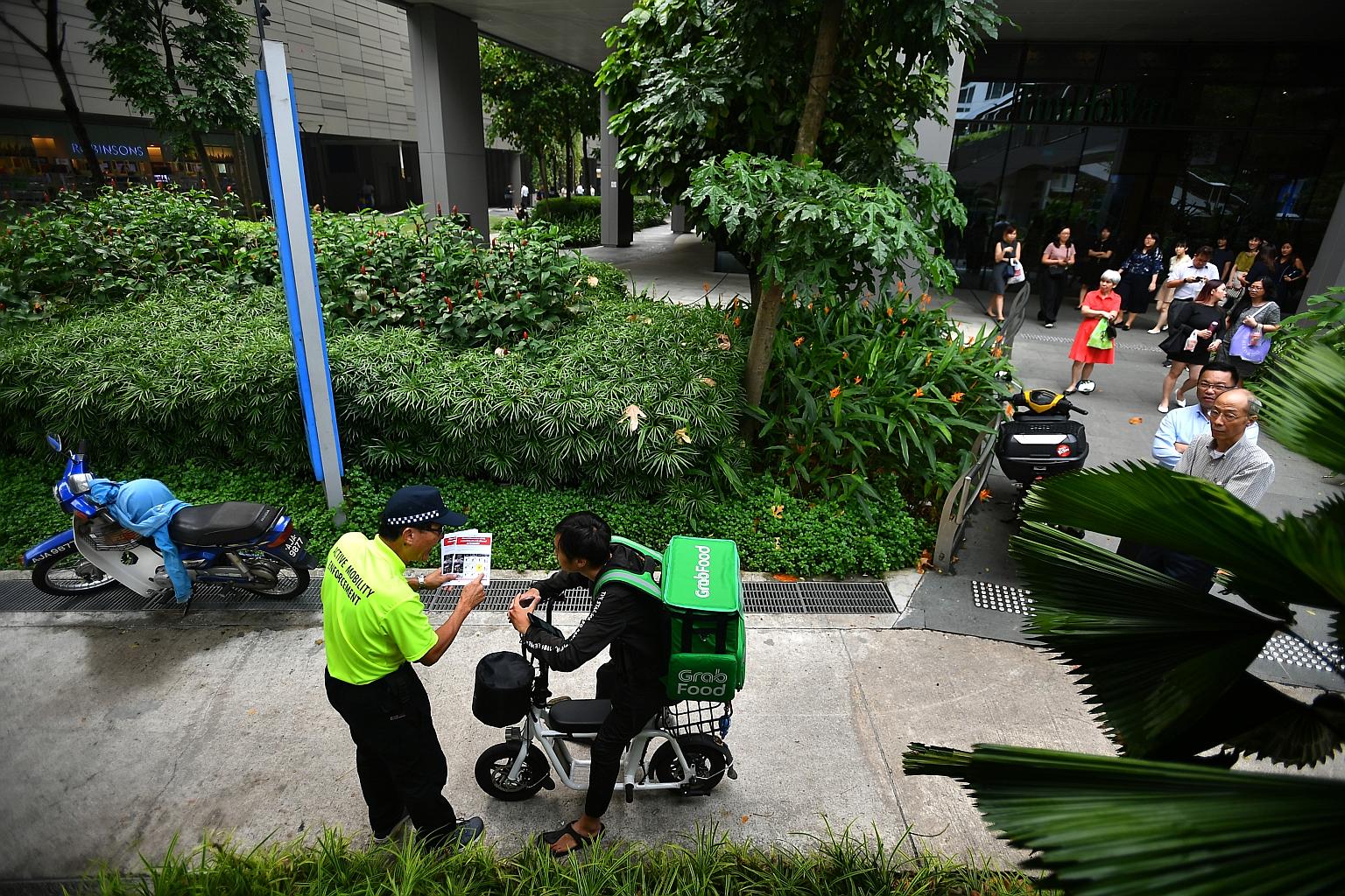 An enforcement officer warning a food delivery rider on his electric scooter on a footpath outside Westgate mall yesterday. The LTA said it will issue warnings to errant riders till Dec 31, but will take "strict enforcement action" in serious cases. 