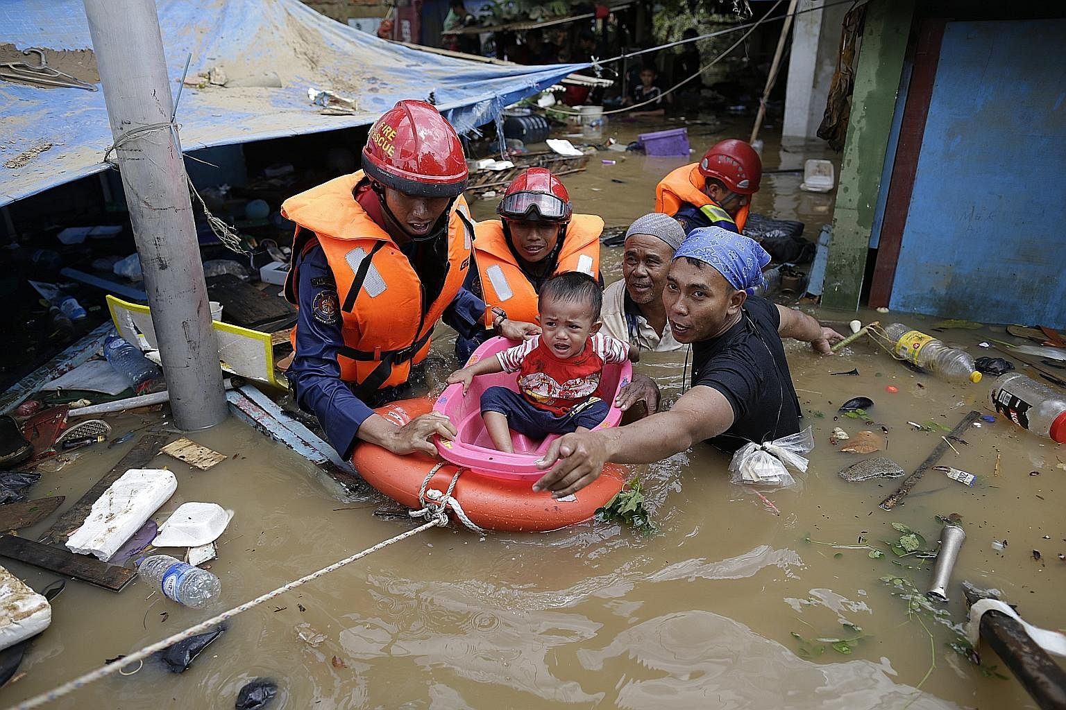 Indonesian rescuers evacuating a boy from a flooded area in Jakarta yesterday. Severe flooding and landslides caused by torrential rain over the New Year period have killed at least 26 people and left thousands more in the Indonesian capital and its 