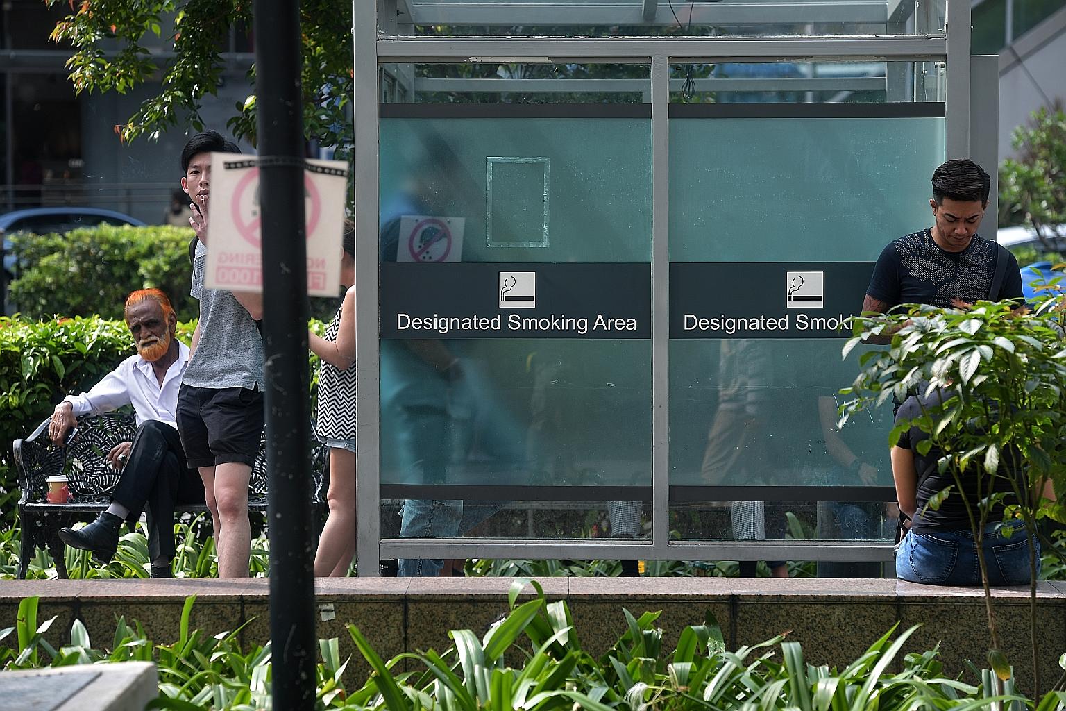 Smokers at a designated smoking area in front of Far East Plaza along Scotts Road yesterday. The National Environment Agency said that an average of 21 tickets per day were issued in the month of April last year - after enforcement began - and the nu