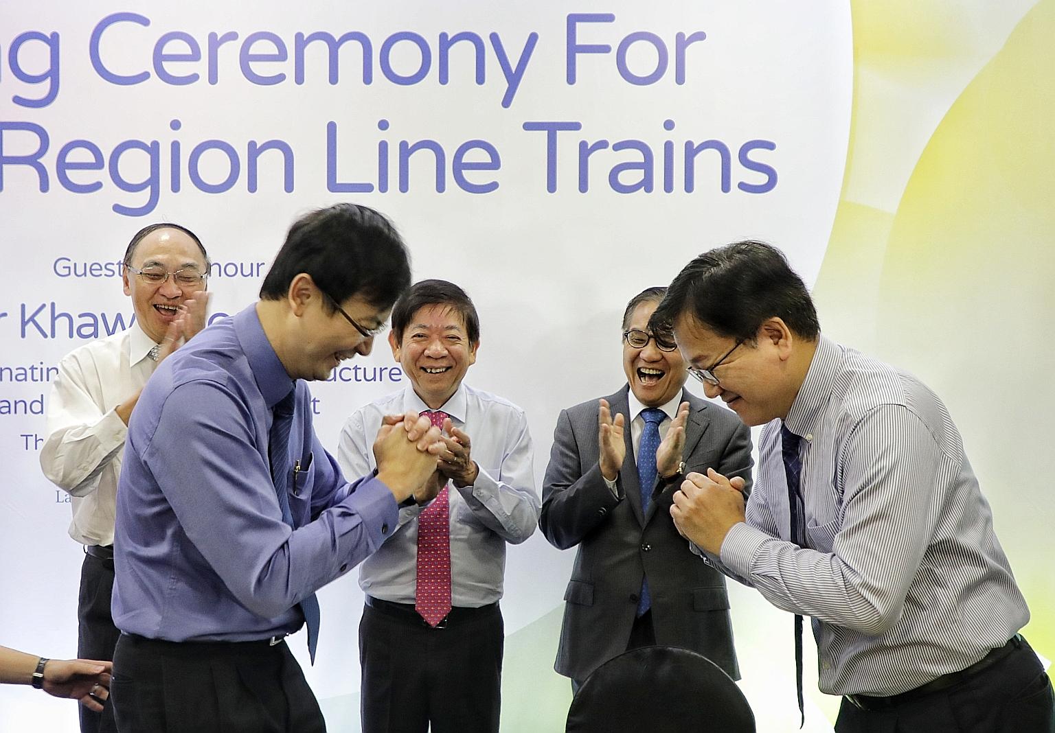 Mr Ngien Hoon Ping (in blue), LTA chief executive, and Mr Choi Dong-hyun, vice-president and chief operating officer of railway business division at Hyundai Rotem, congratulating each other after the signing ceremony. Looking on are (from left) LTA c