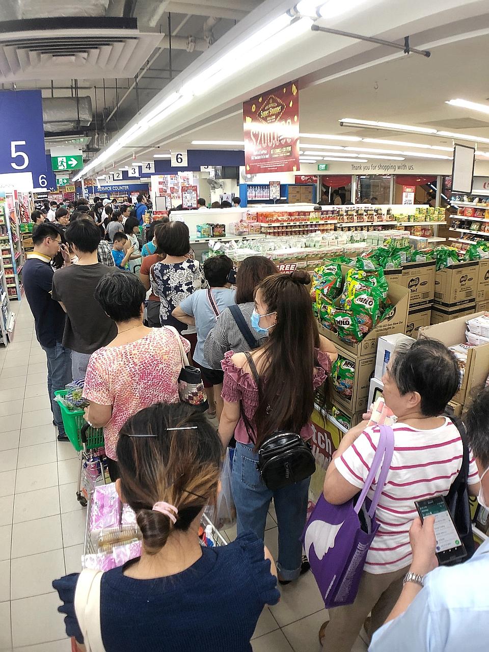 Shoppers queueing to pay for essential items at the FairPrice supermarket at HDB Hub in Toa Payoh yesterday. Items began flying off the shelves at some supermarkets here after Singapore announced earlier in the day that it would be raising its diseas
