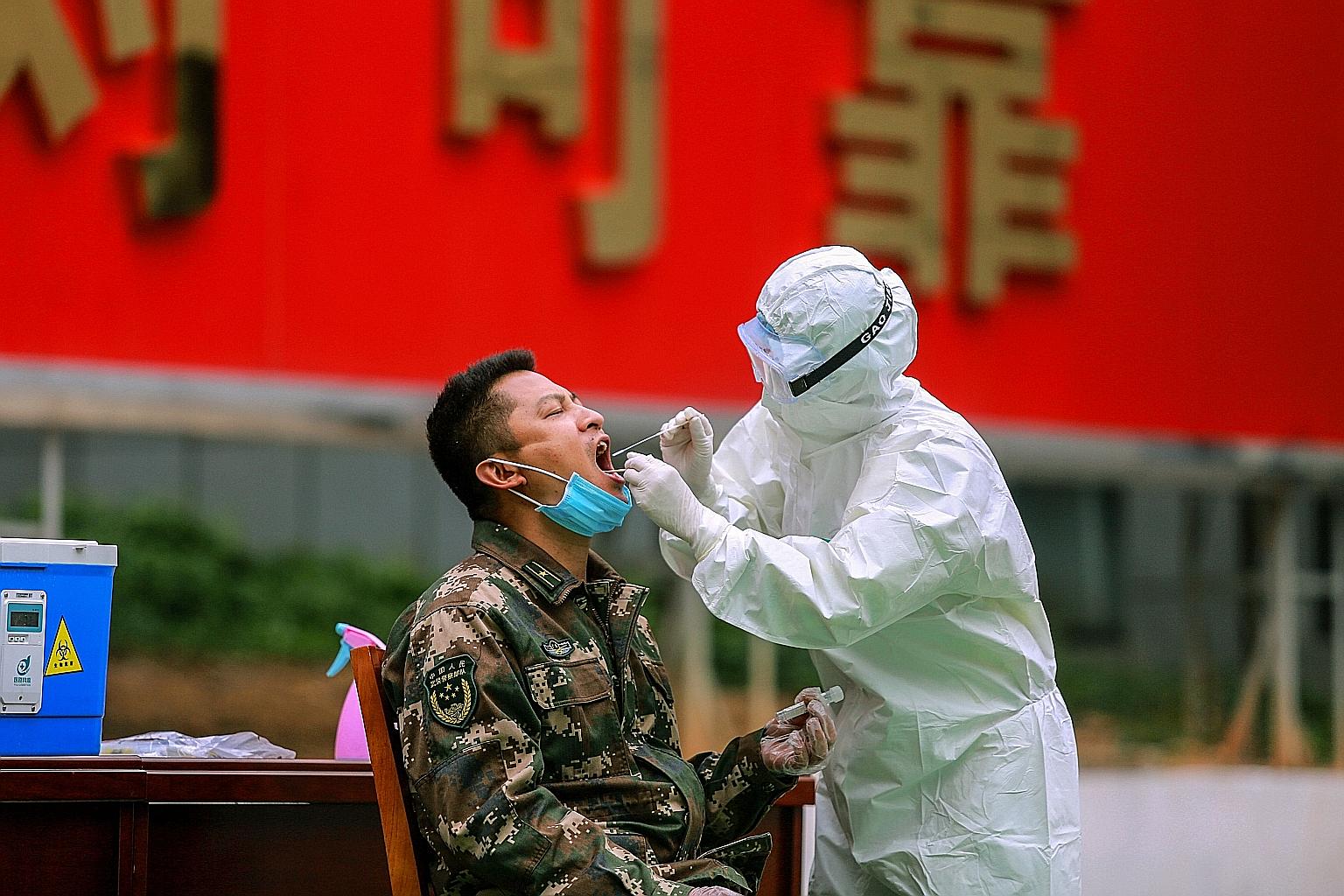 A medical staff member collecting a sample from a Chinese paramilitary police officer for coronavirus testing on Tuesday after his return from a holiday in Shenzhen, in China's southern Guangdong province.
