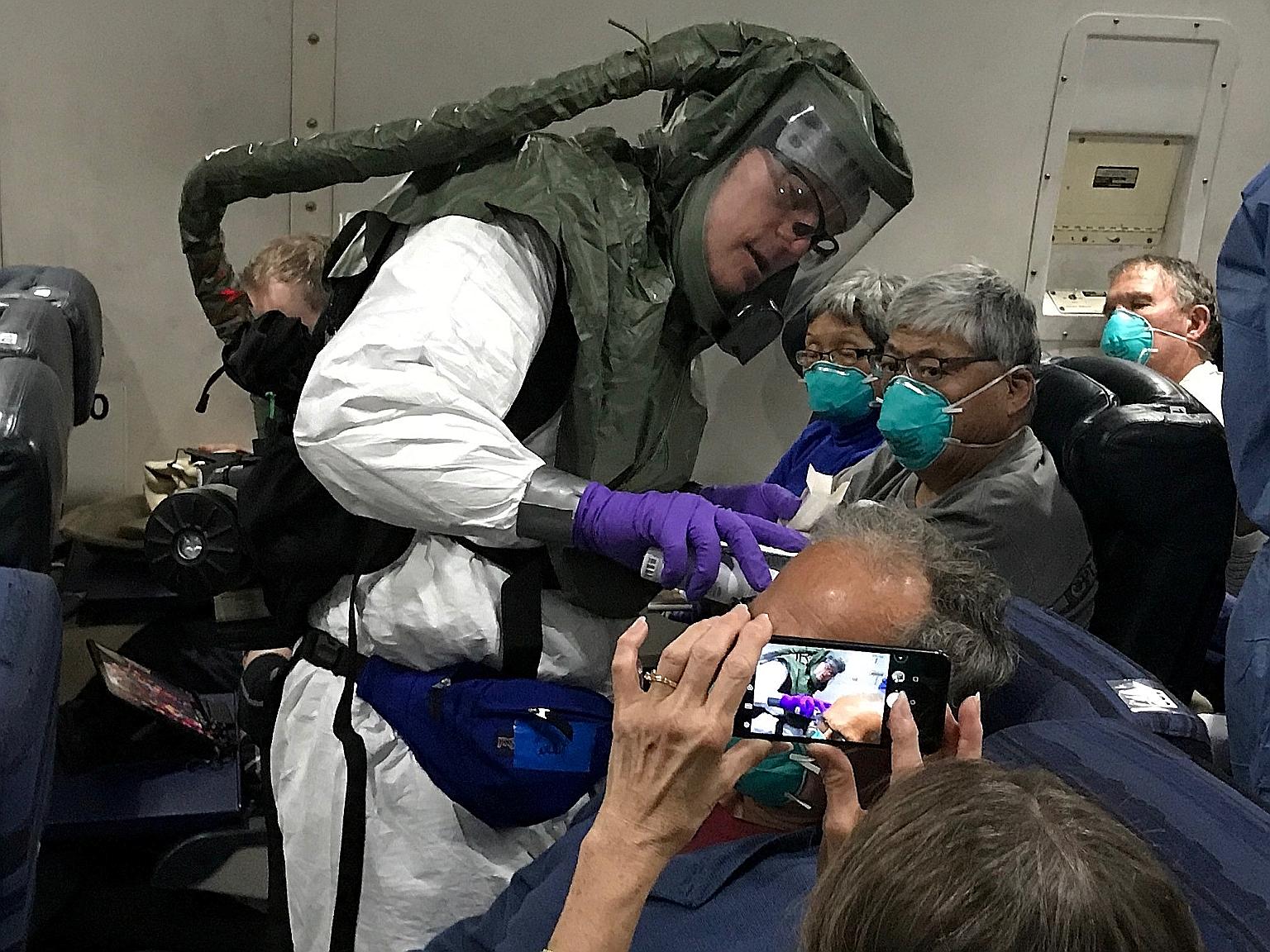 A worker in a protective suit checking the temperatures of passengers who were on board the Diamond Princess cruise ship, on a chartered evacuation aircraft from Tokyo's Haneda Airport, en route to Lackland Air Force Base in the US on Monday.
