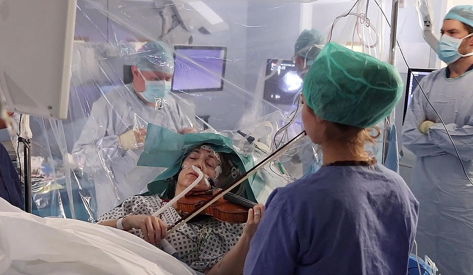 An image from video footage showing violinist Dagmar Turner playing the violin as doctors monitored her movements on screens during her brain surgery on Jan 31. She helped surgeons avoid damage to her brain during the operation to remove a tumour by 