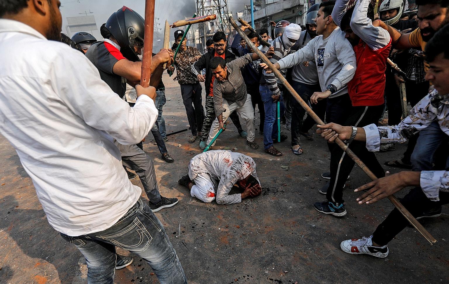 Above: A widely shared photo of a bloodied man on the ground surrounded by attackers in New Delhi on Monday. Left: Men pelting stones and starting fires during clashes in eastern Delhi between groups for and against India's Citizenship Amendment Act.