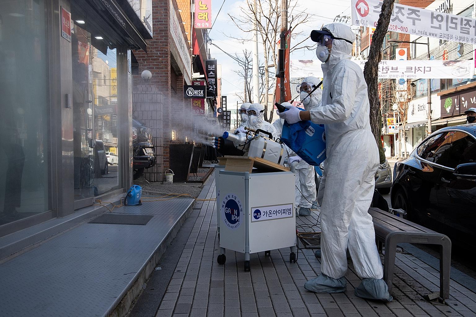 People queueing to buy masks supplied by the government at a department store in the Mokdong district of Seoul yesterday. Workers in protective suits spraying disinfectant on a store window in Munjeong-dong Rodeo Street in the Songpa district of Seou