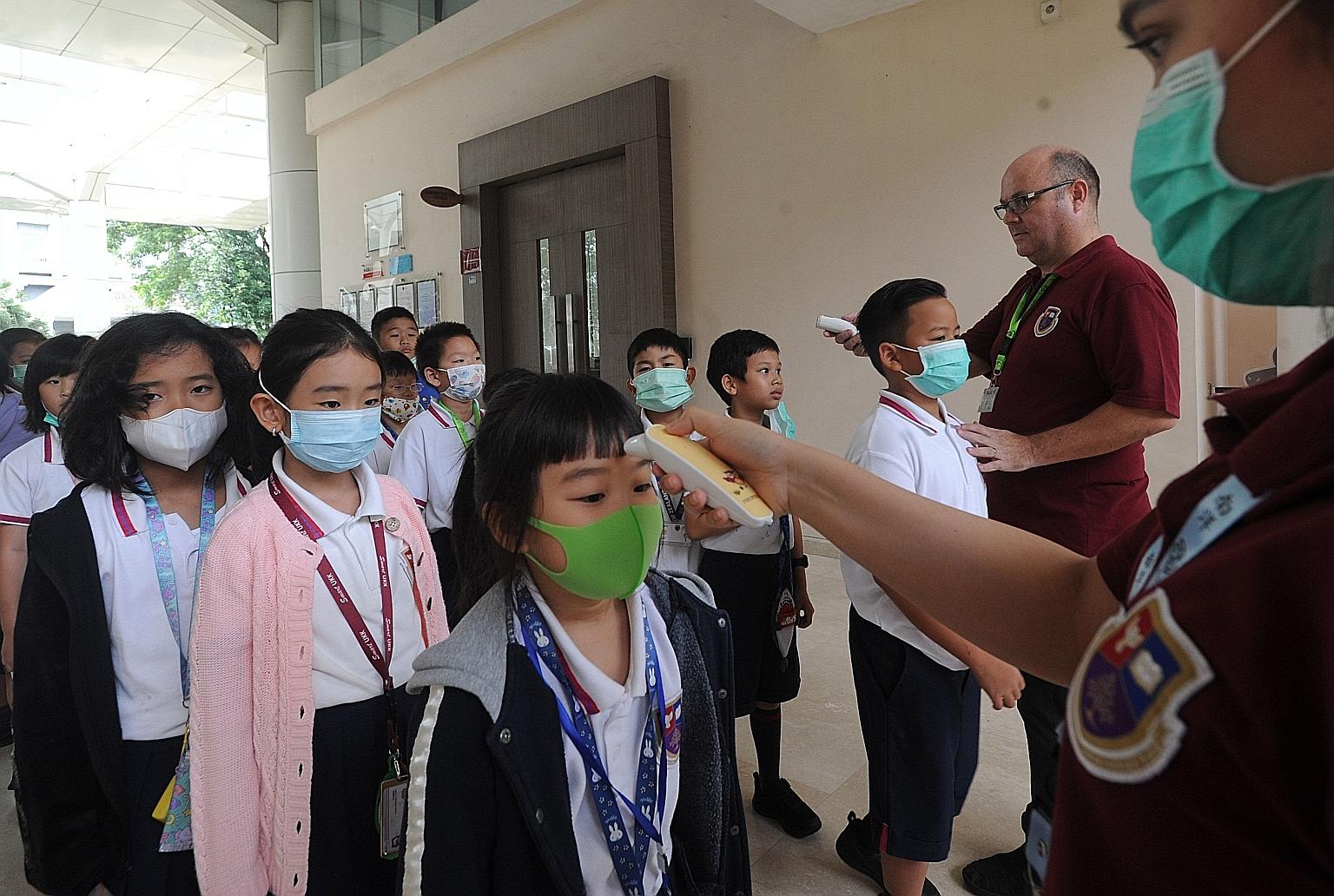 School officials checking the temperature of students before they entered a school in Tangerang, Indonesia, yesterday. PHOTO: AGENCE FRANCE-PRESSE