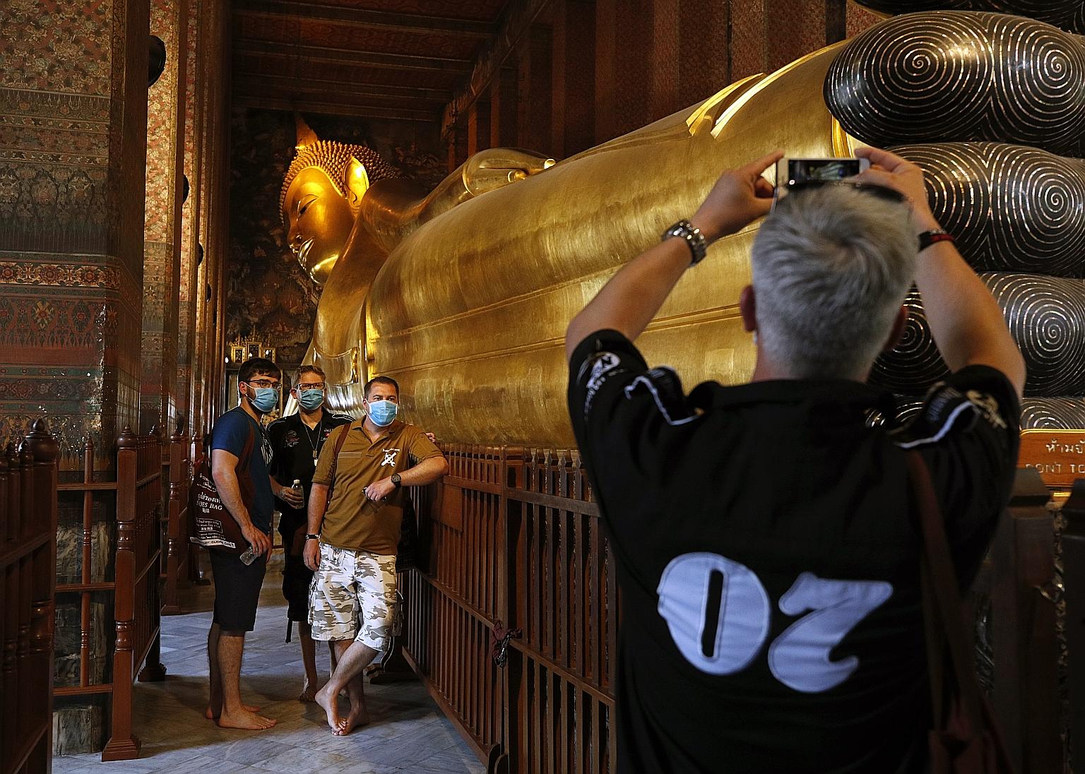 Foreign tourists having their photo taken next to the Reclining Buddha statue at Wat Pho temple in Bangkok last Friday. With the new infections, Thailand now has 114 coronavirus cases, with one death.