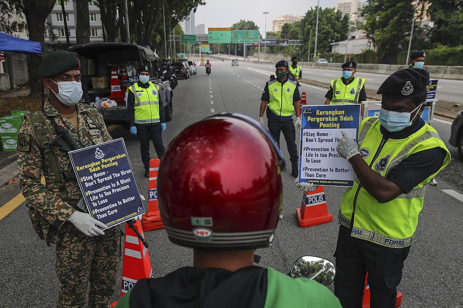 A Malaysian soldier and a police officer reminding a motorcyclist at a roadblock in Kuala Lumpur yesterday about the 14-day partial lockdown in the country. It was the first day that thousands of military men were out on the streets to implement Mala