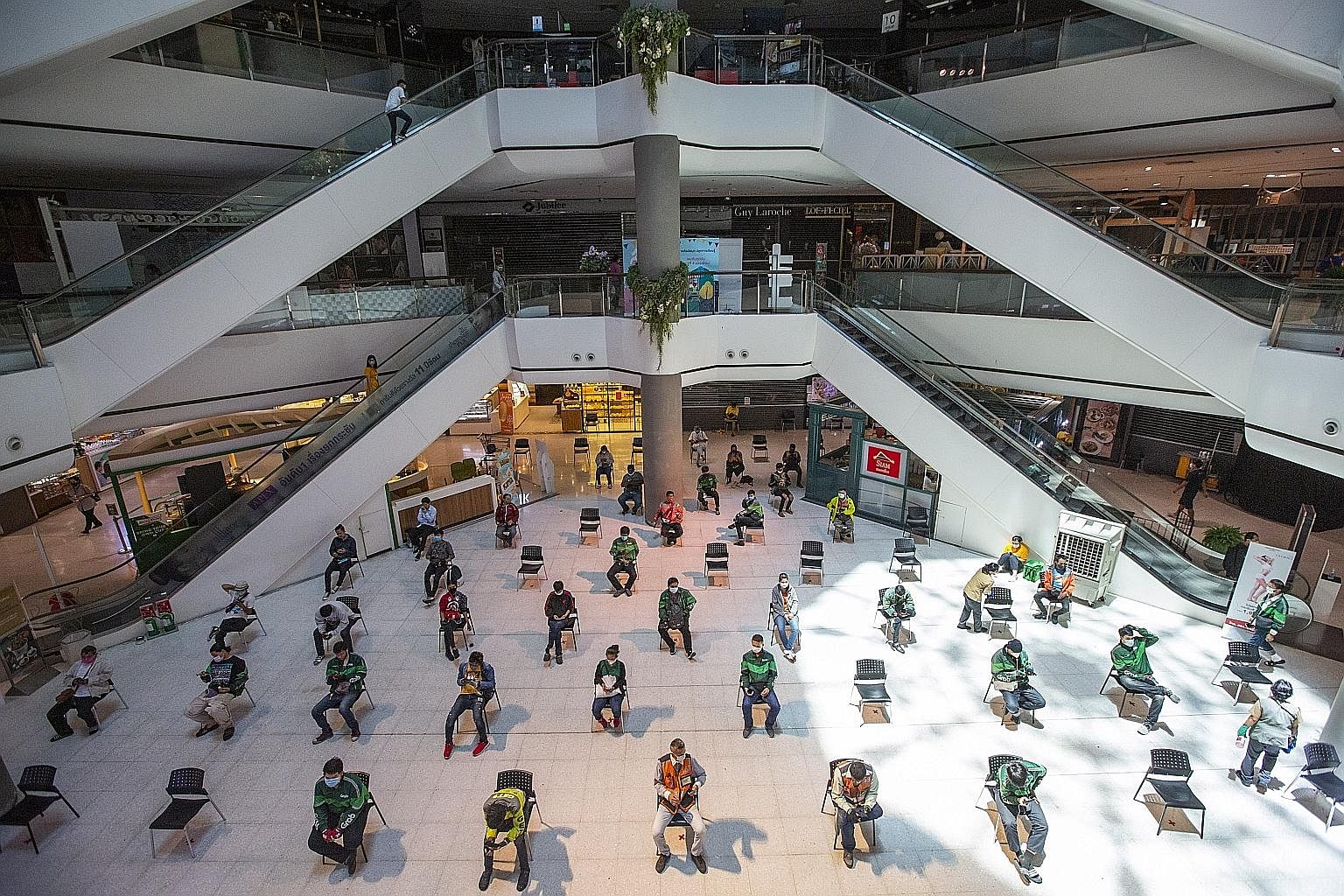 Food delivery couriers keeping a distance from one another while waiting at the Central Plaza Pinklao mall during a partial lockdown in Bangkok yesterday. With over 1,500 cases of coronavirus infections recorded in Thailand so far, even relaxed folk 