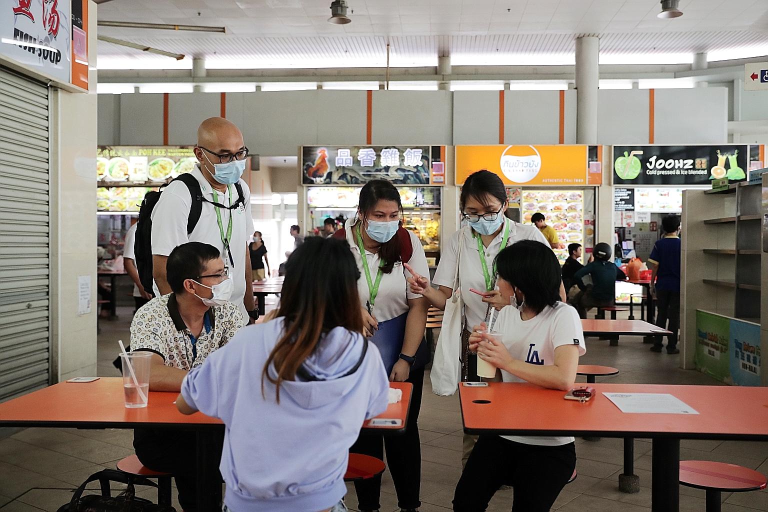 National Environment Agency officers advising members of the public on the stricter safe distancing rules at Bedok Interchange Hawker Centre yesterday. ST PHOTO: GIN TAY