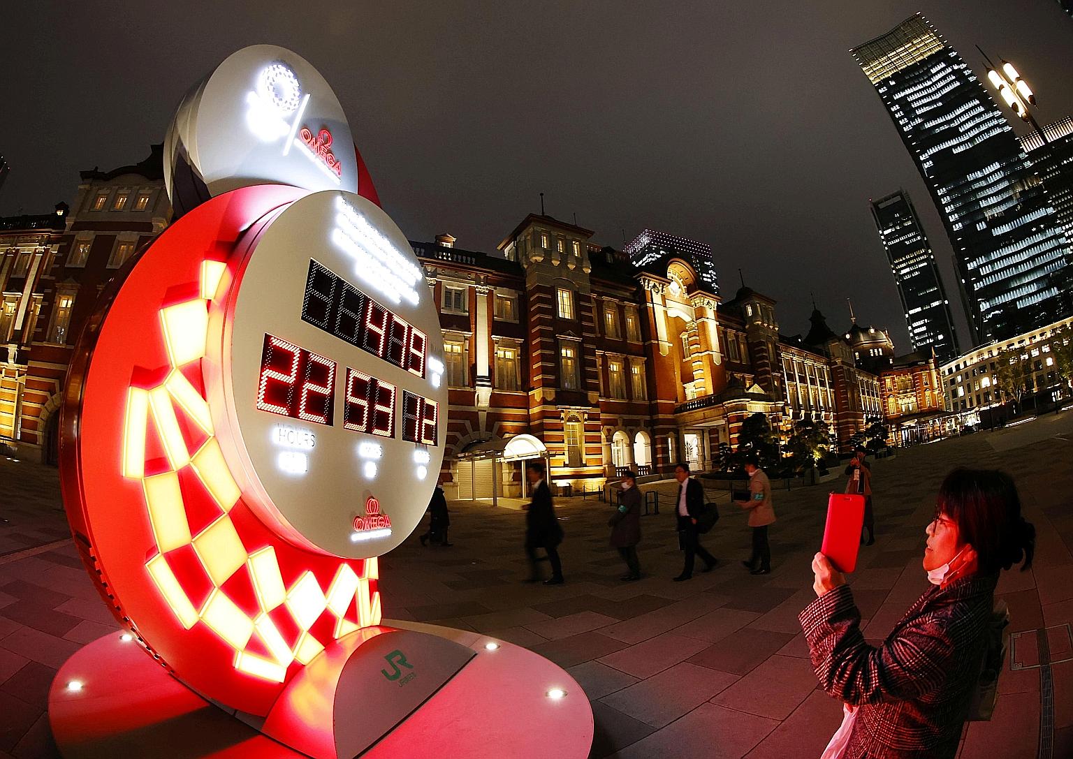 A woman taking photos of a countdown clock showing the adjusted days and time till the start of the postponed Tokyo Olympics in front of the Tokyo Station on March 30. The Games are now set to begin on July 23 next year. PHOTO: REUTERS