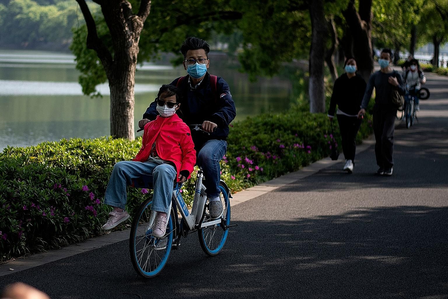 From top: Cyclists and walkers in Wuhan's East Lake Plum Flower Garden on Sunday, after the city's lockdown ended; medical workers outside Jinyintan Hospital last Tuesday; employees in protective gear disinfecting a visitor to the city's Zonsen Medic
