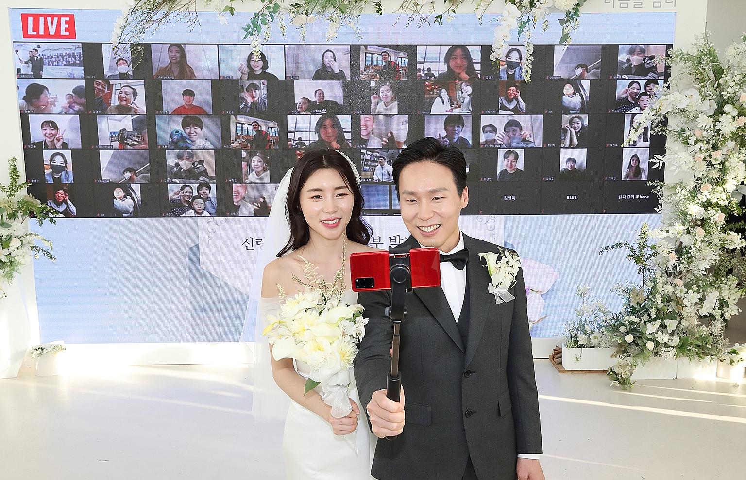 Groom Ha Ji-soo and bride Park Ji-ye posing for a wefie as they live-streamed their wedding from Seoul on April 4, with family and friends (background) logged on to watch and interact with the couple.