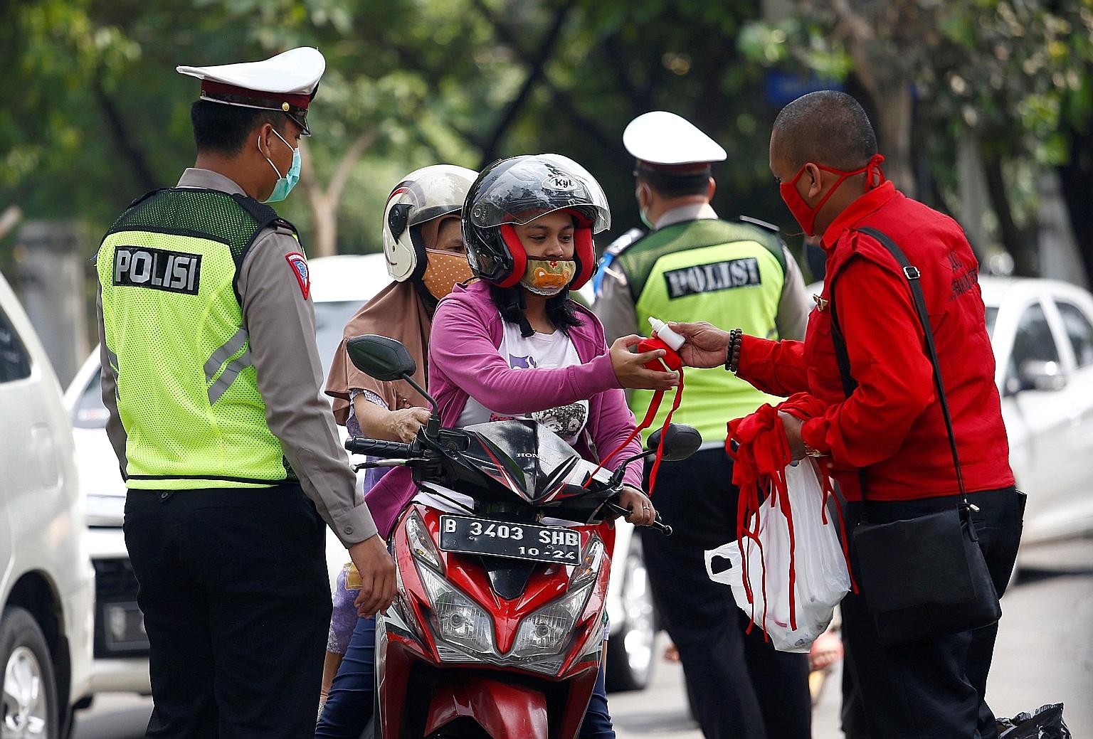 A police officer in Depok, a city in Indonesia, looking on as a motorcyclist receives a mask and hand sanitiser to prevent the spread of Covid-19. PHOTO: REUTERS