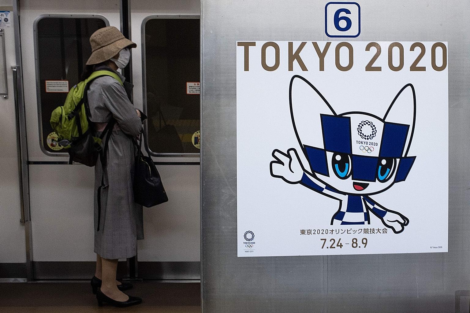 A passenger wearing a face mask stands next to a poster of Tokyo 2020 Olympic mascot Miraitowa on a train in Tokyo. The cost of rescheduling the Games to July 23-Aug 8 next year is estimated at S$4.3 billion, said Kyodo news agency. PHOTO: AGENCE FRA