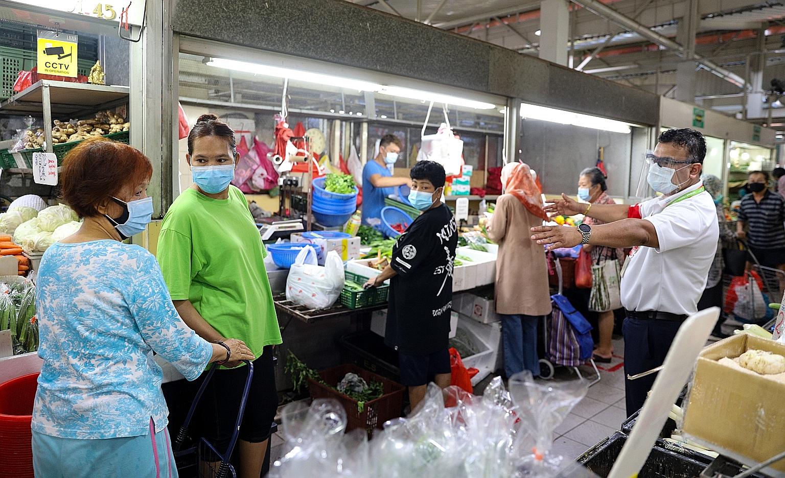 An SG Clean ambassador (right) ensuring shoppers at the wet market at Marsiling Lane adhere to safe distancing rules at around 10.20am yesterday. Despite it being an even date, meaning only shoppers whose NRIC number has an even last digit can enter,