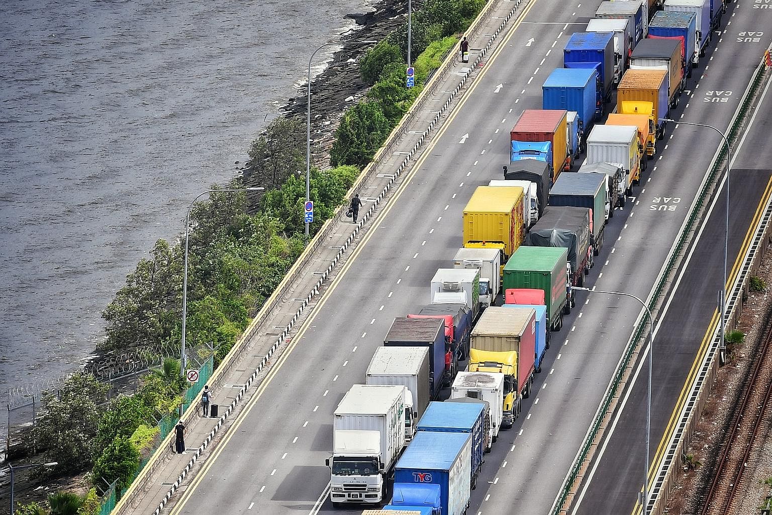 Malaysian workers walking across the Causeway towards Johor with their luggage yesterday morning, passing by trucks carrying goods into Singapore. Johor health and environment committee chairman R. Vidyananthan said that effective yesterday, up to 40