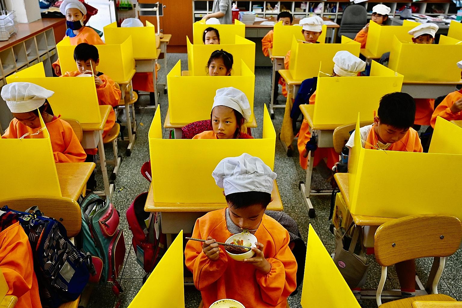 Pupils eating lunch at their desks with plastic partitions put up as a preventive measure against the coronavirus at an elementary school in Taipei yesterday.
