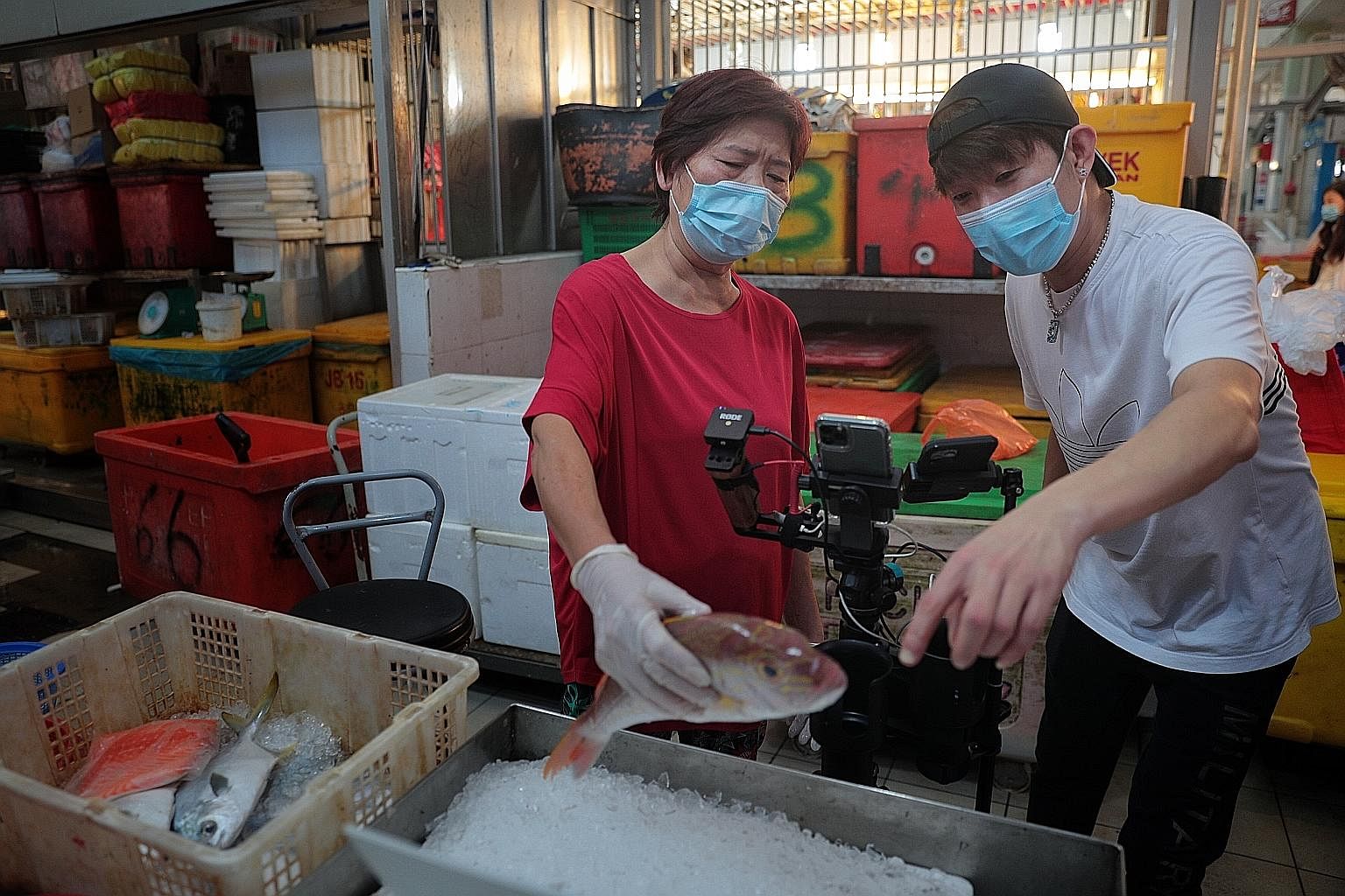 Ms Janet Tiou, 68, of the 81 Sheng Yu stall at Tekka Market received some tips on selling her seafood on a livestream yesterday from Mr Max Kee, 37, of Lian Huat Seafood. Yesterday was the first day of a new initiative to take the wet market shopping