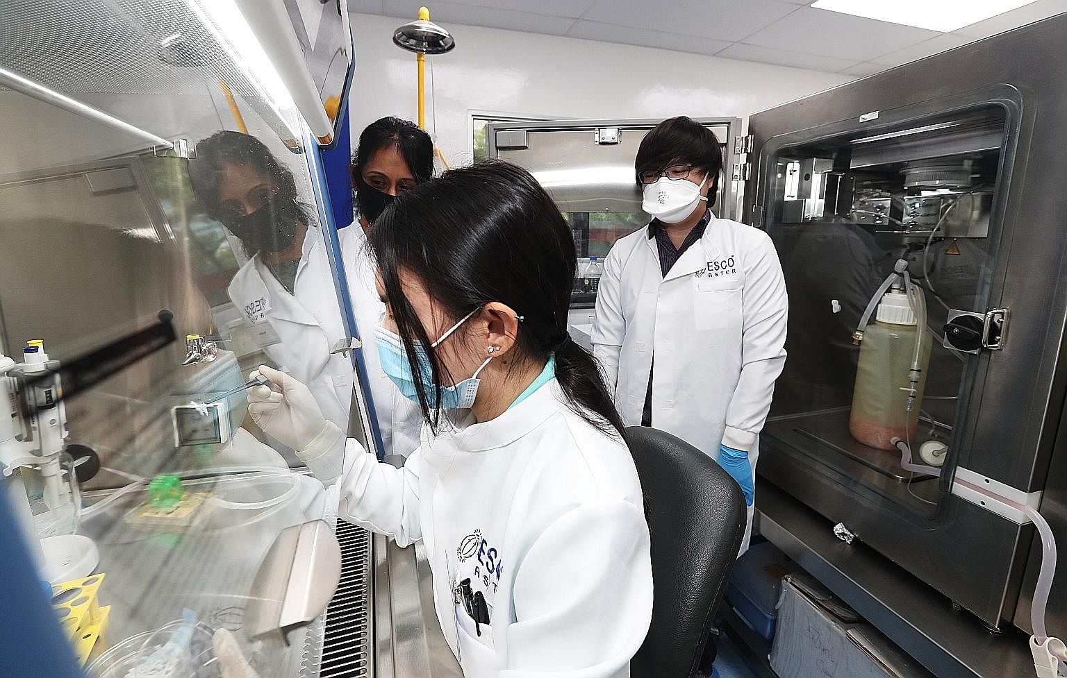 (Clockwise from foreground) Esco Aster research officer Micaela Goh, senior bioprocess scientist Nandini Prabhakar and CEO Lin Xiangliang in the firm's lab. On the right is the bioreactor used to culture the vaccine.