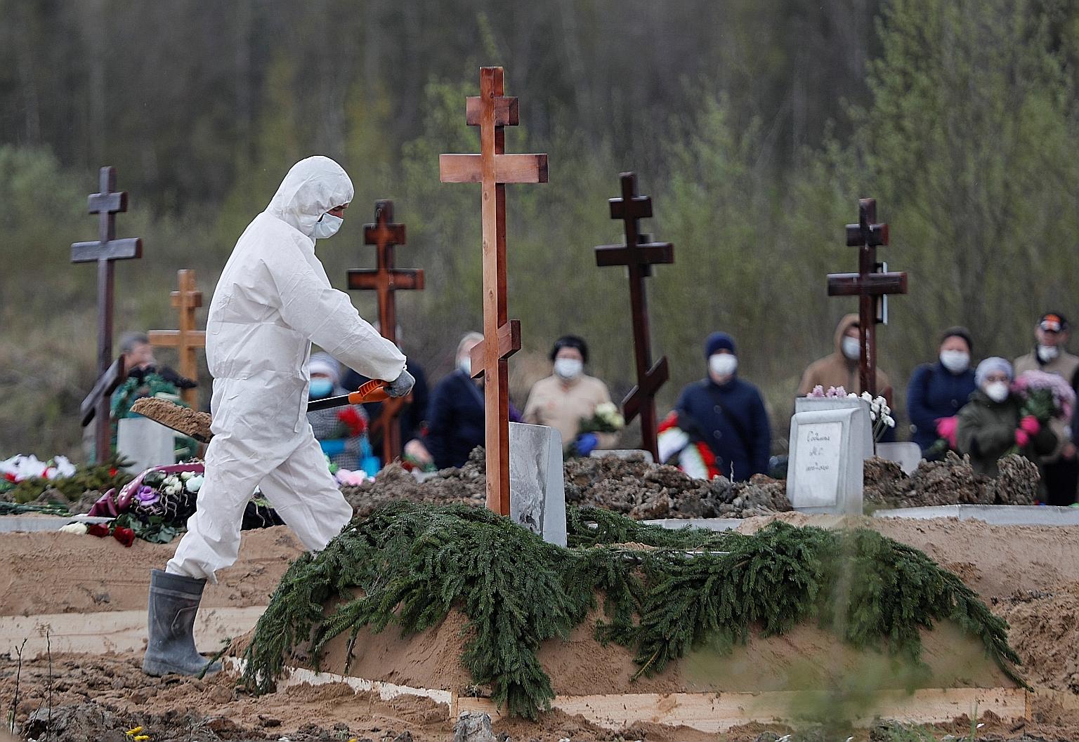 A gravedigger wearing personal protective equipment yesterday in St Petersburg while burying a person who is presumed to have died from Covid-19, with mourners in masks standing at a distance. Russia has almost 250,000 confirmed coronavirus cases, bu