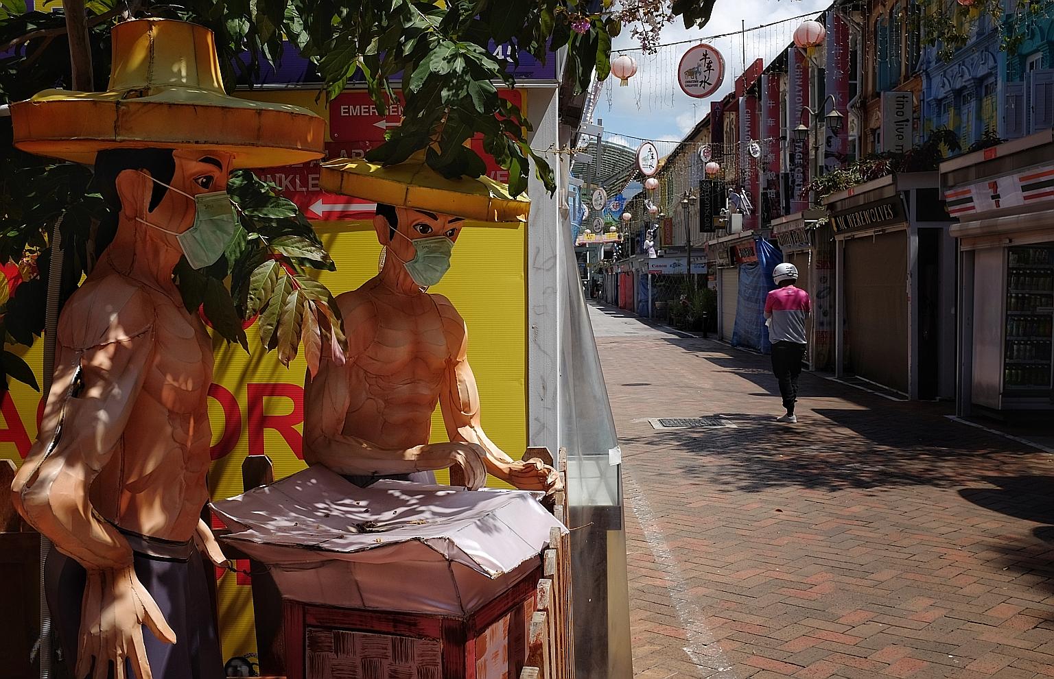 Figures of coolies along a street in Chinatown sporting masks yesterday. The streets of the colourful district, usually bustling with tourists and locals, have been quiet during the circuit breaker, though some activity has returned with the reopenin