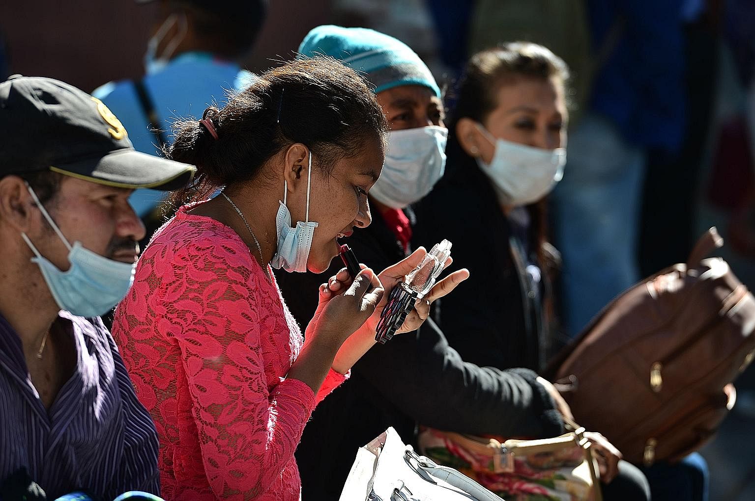 A woman applying lipstick next to people wearing face masks amid the coronavirus outbreak, in Tegucigalpa, Honduras, in March. With face coverings an inevitable part of our essential attire for some time to come at least, some are wondering about the
