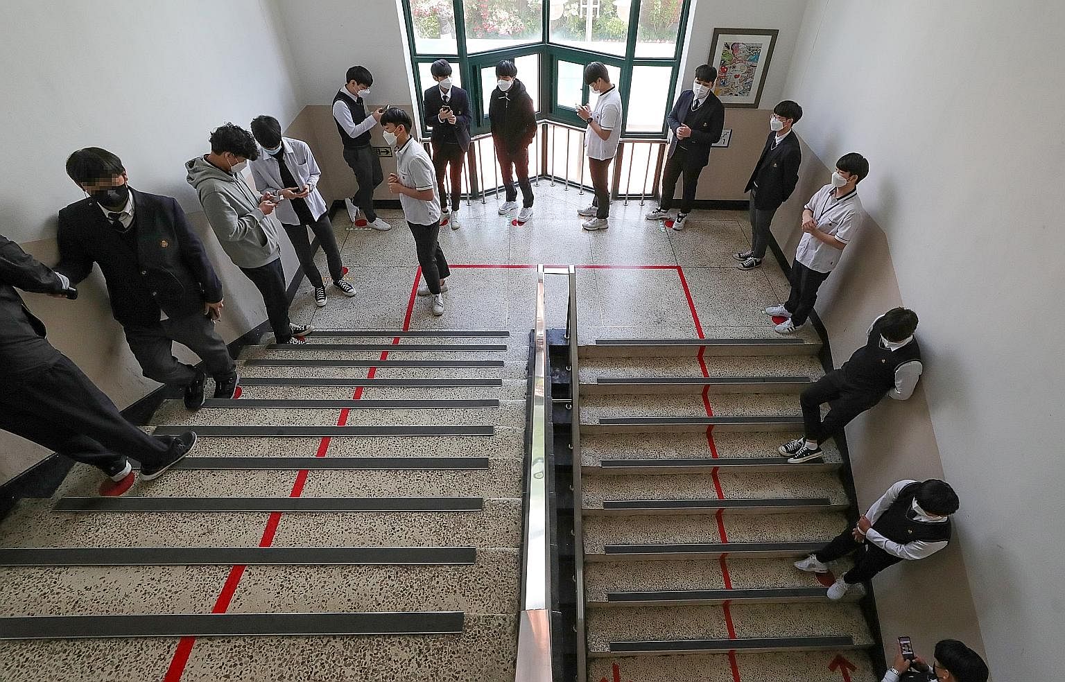 Above: High school seniors sitting behind protective shields as a preventative measure against the coronavirus in a classroom in Daejeon, South Korea, yesterday. Below: Some seniors standing in line to enter the cafeteria as high schools nationwide r