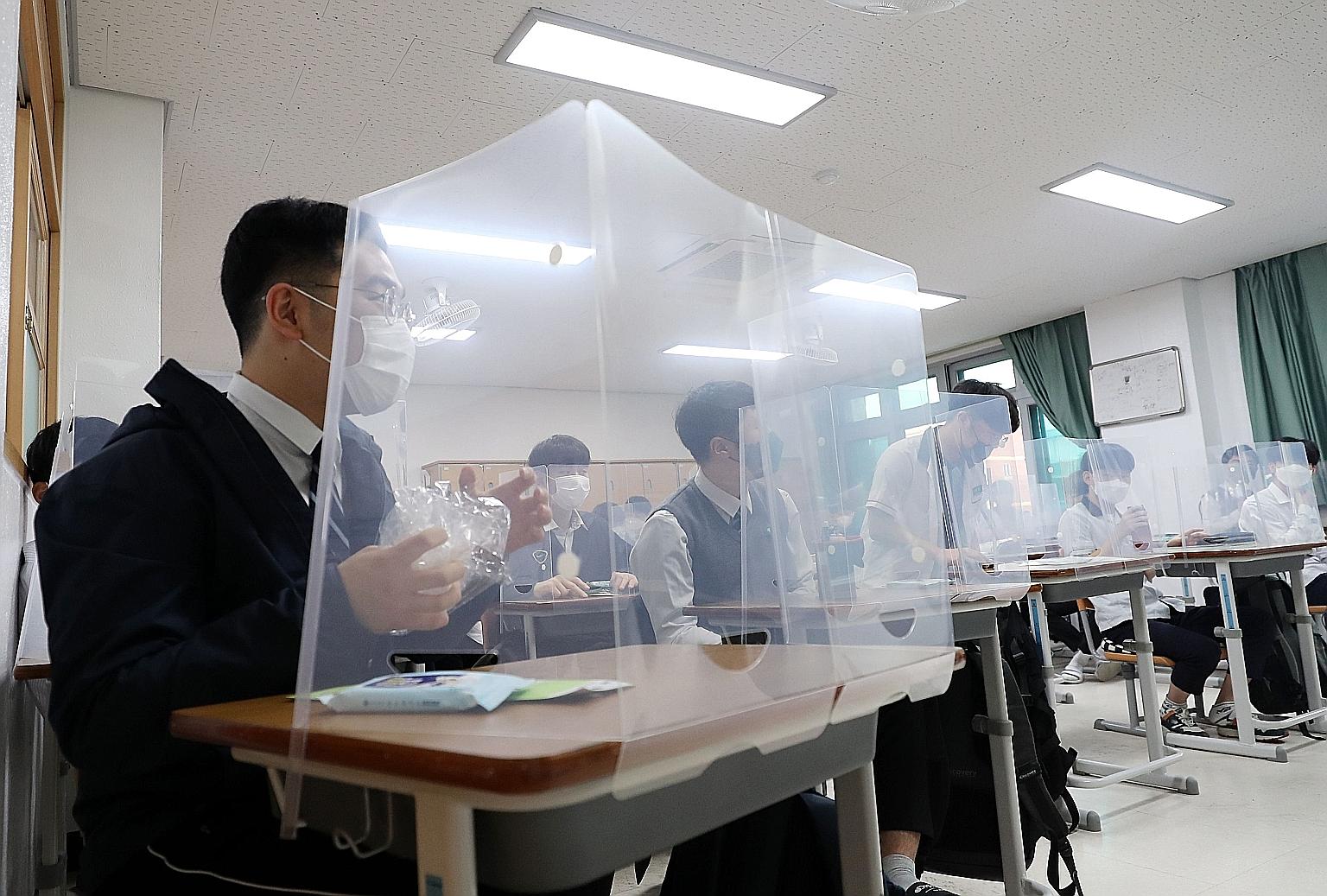 Above: High school seniors sitting behind protective shields as a preventative measure against the coronavirus in a classroom in Daejeon, South Korea, yesterday. Below: Some seniors standing in line to enter the cafeteria as high schools nationwide r