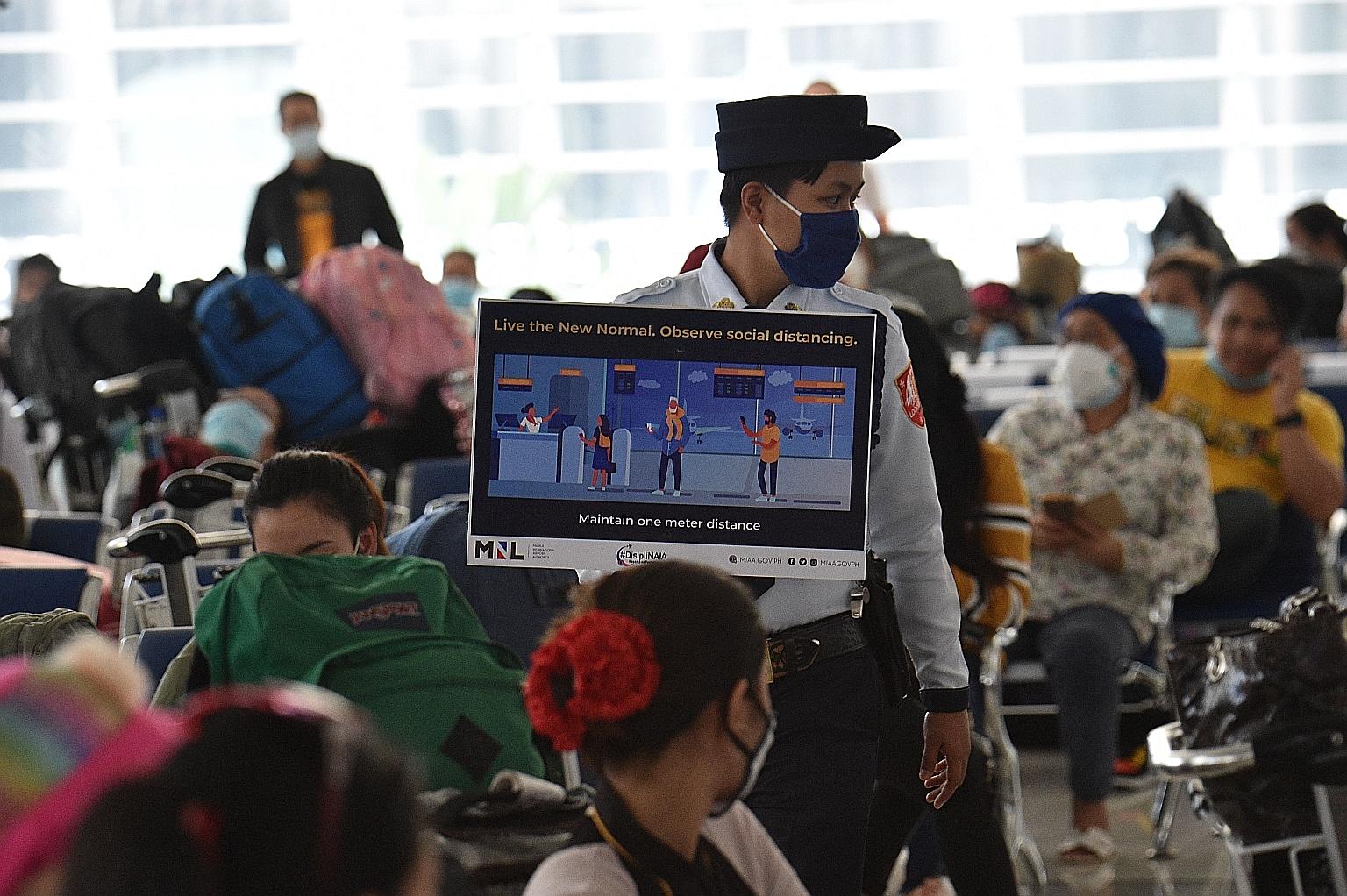 A security guard at Manila's international airport reminding people of social distancing measures yesterday as Philippine overseas workers waited for flights back to their home cities. PHOTO: AGENCE FRANCE-PRESSE