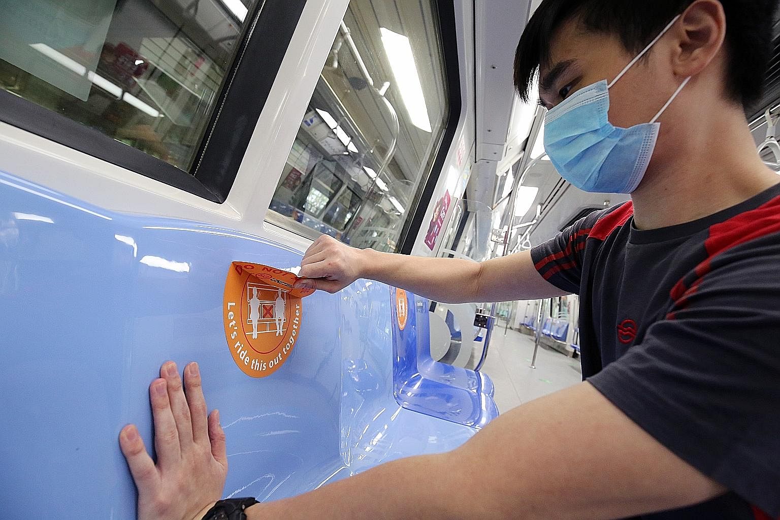 An SMRT employee removing a safe distancing sticker from an MRT train seat yesterday ahead of the end of the circuit breaker. The stickers are being removed as physical distancing on trains and buses will be hard once crowds return. Seat markers will