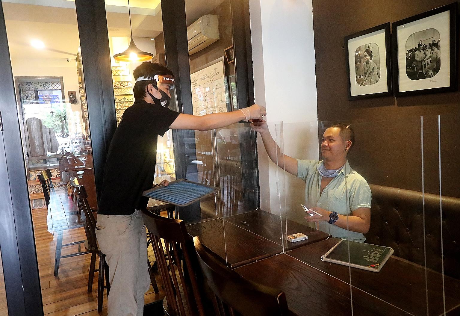 An employee in protective gear delivering a drink to a customer in an eatery in Jakarta on Thursday. The Indonesian capital's efforts to reopen its economy come as the rates of infection both in Jakarta and across the country appear to be acceleratin