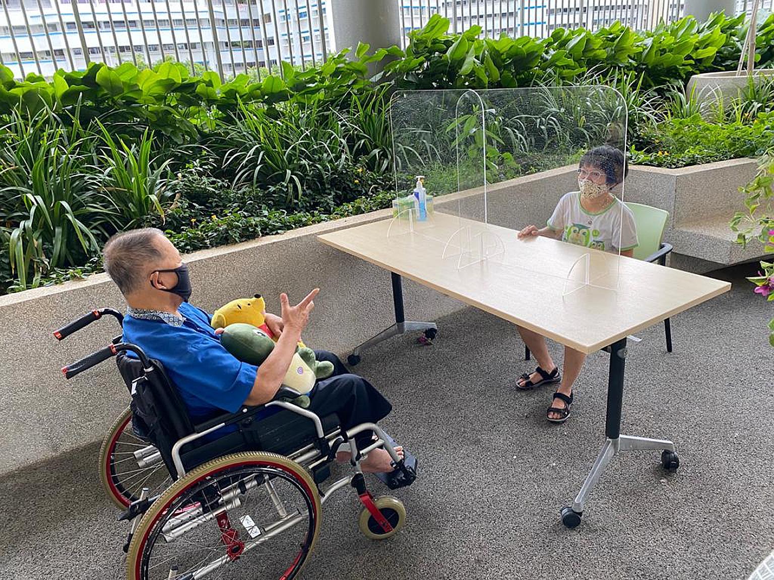 Ms Grace Ang, 39, visiting her father Ang Tiak Huat, 72, at NTUC Health Nursing Home (Geylang East). Clear acrylic partitions separating visitors from residents help to minimise the risk of droplets spreading. PHOTO: NTUC HEALTH