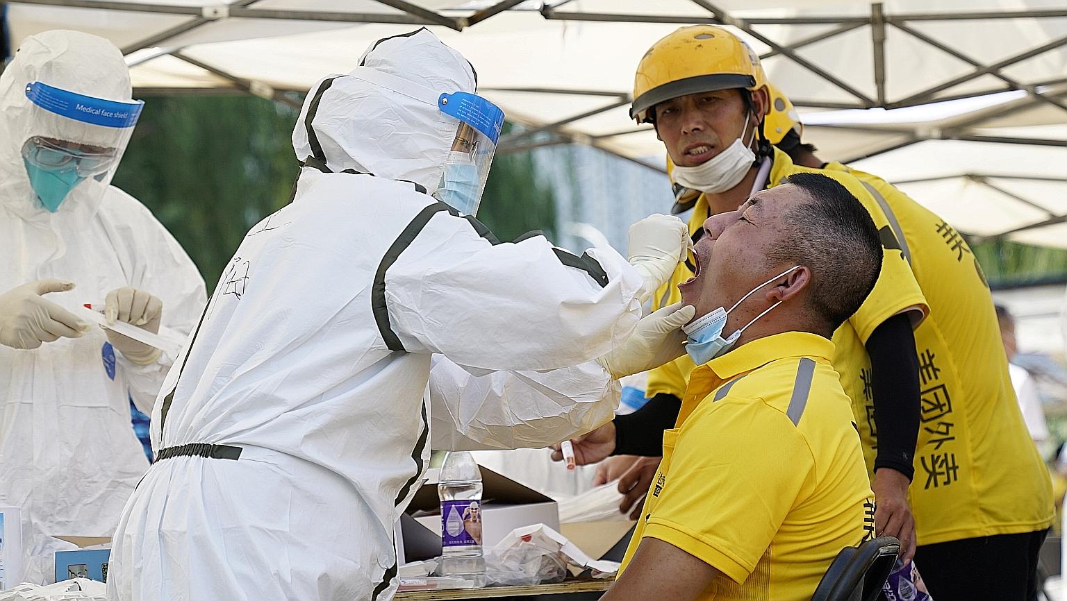 Medical workers conducting a nucleic acid test yesterday on a food delivery worker from Meituan Dianping, following a new outbreak of Covid-19 in Beijing, which has now surpassed previous peak numbers in the city in early February. Residents of 40 co