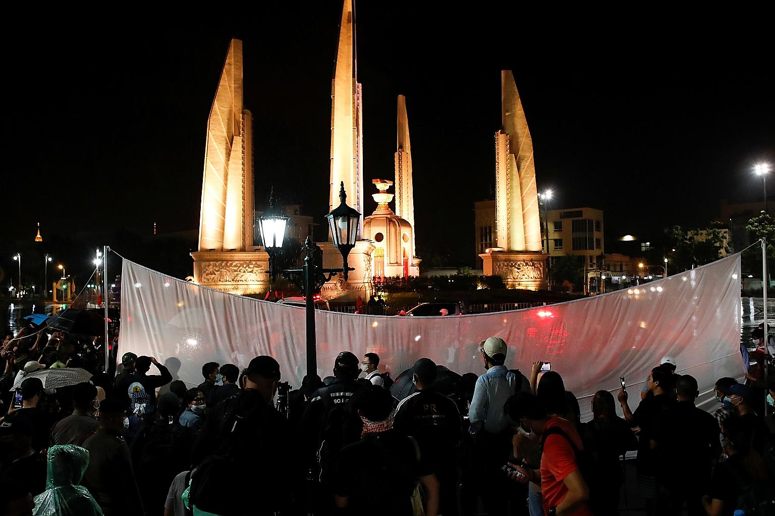 Thai pro-democracy protesters place a white screen in front of the Democracy Monument in Bangkok, calling yesterday for change to the constitution on the 88th anniversary of a revolt that ended Thailand's absolute monarchy.