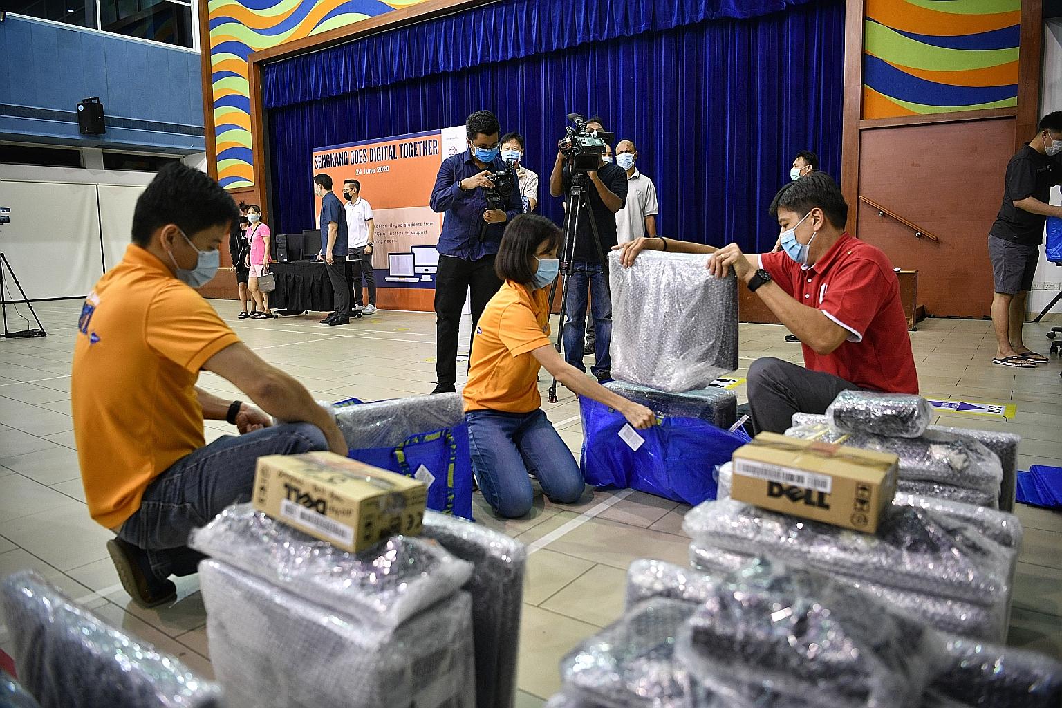 Minister in the Prime Minister's Office Ng Chee Meng helping volunteers place computers into bags before giving them out to recipients at the launch of a programme to help students from low-income families, at Anchorvale Community Club yesterday.