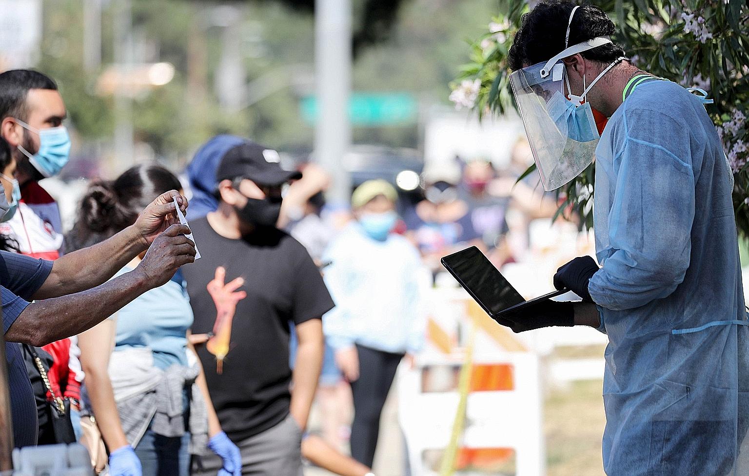 A healthcare worker in personal protective equipment helping people waiting in line to check in at a Covid-19 testing centre at Lincoln Park in Los Angeles last Tuesday.