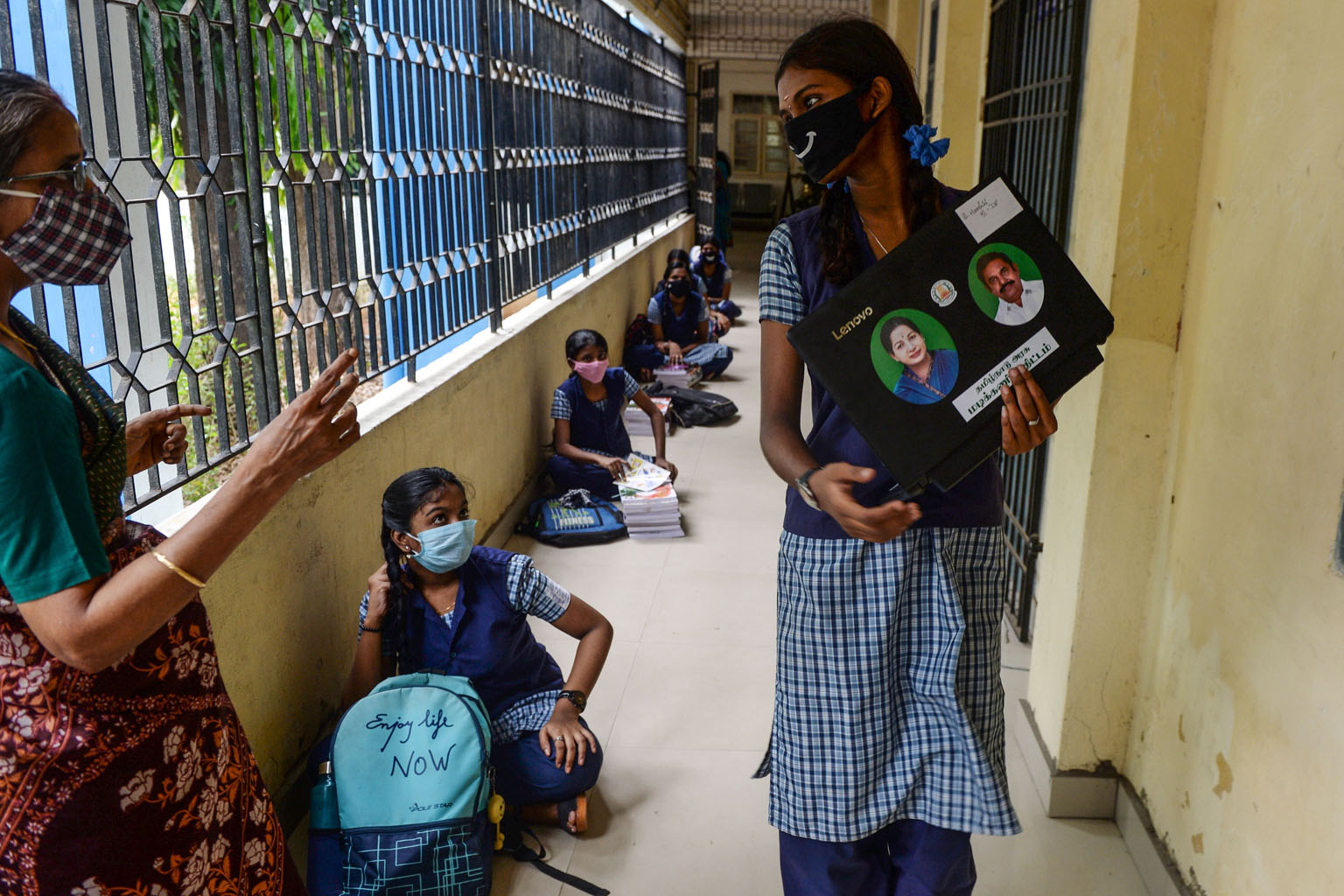 A student carrying a laptop to download study materials, while others lined up to collect textbooks before attending a tele-learning class at home last week in Chennai.