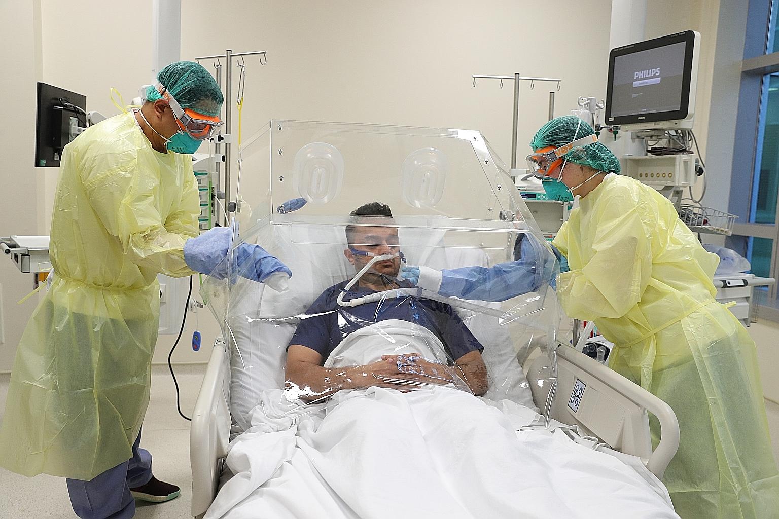 A staff member of Ng Teng Fong General Hospital acting as a patient to demonstrate how one of the box shields enables non-sedated patients to be propped up on bed, providing more comfort, during treatment.