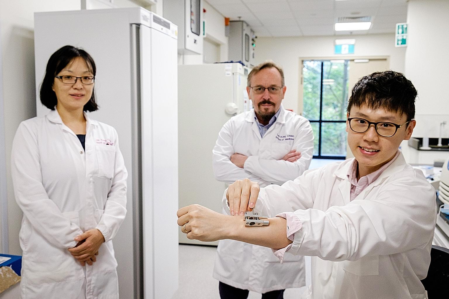 A*Star's Dr Daniel Lio (right) demonstrating his team's prototype device that uses two magnets to create temporary micropores to administer drugs more efficiently through the skin. With him are team members Wang Xiaomeng and David Laurence Becker of 