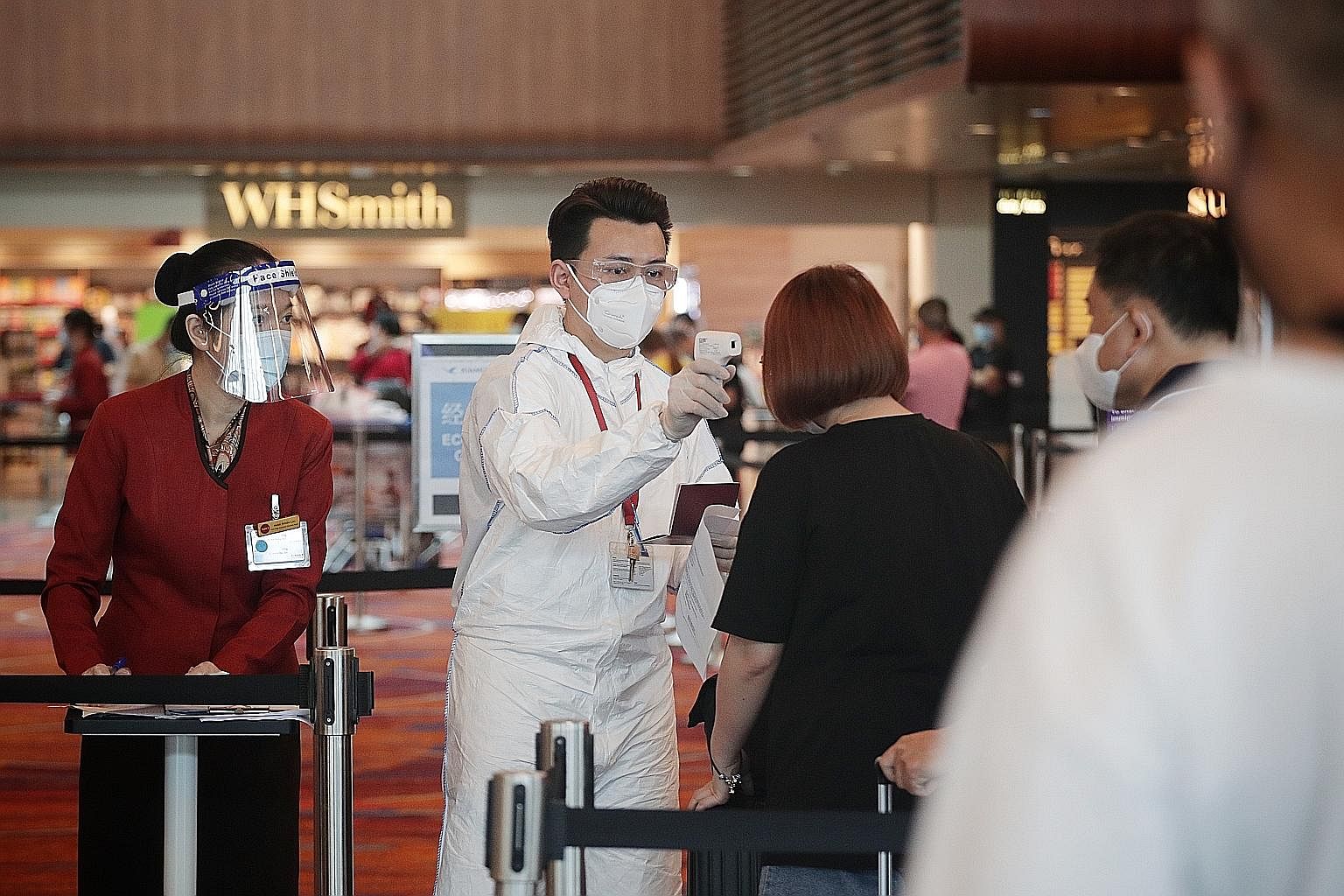 Airport staff taking the temperature of a traveller checking in for a flight at Changi Airport Terminal 1 earlier this month. Staff at the airport will be put on rostered routine testing similar to front-line workers and migrant workers.