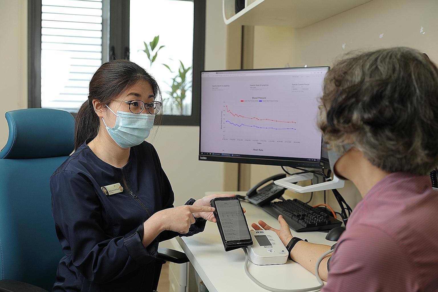 Ang Mo Kio Polyclinic care coordinator Hazel Yang showing Madam Tham Siew Yee how the app works. Patients like Madam Tham take their blood pressure readings at least once a week with a Bluetooth-enabled monitoring device, which automatically transmit