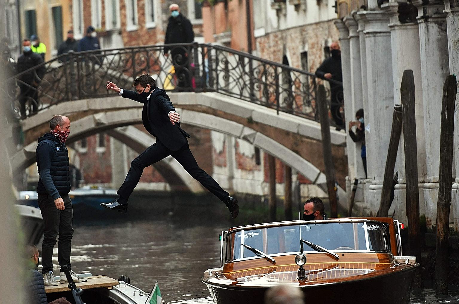 In this file photo taken in October, actor Tom Cruise (centre), with mask on, jumps between two taxiboats during the shooting of the film Mission Impossible: Lybra in Venice.